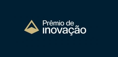 ilustração sob fundo azul marinho com a frase “Prêmio de Inovação” na cor branca, ao centro. Do lado esquerdo da frase, símbo