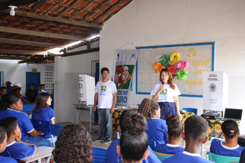 No auditório, servidores Silas e Ludmila apresentando o Eleitor do Futuro.