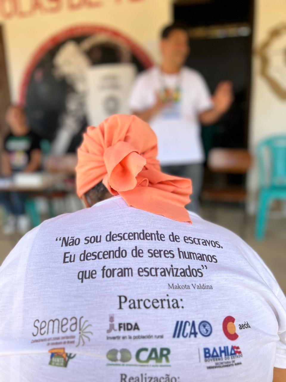 Mulher negra. Frase de efeito na camisa: Não sou descendente de escravos.Eu descendo de seres humanos que foram escravizados.